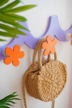 a straw purse hanging on the wall next to a potted plant and some fake flowers