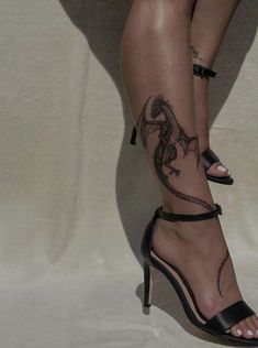 a woman's legs with tattoos and high heels on her feet, both wearing black sandals