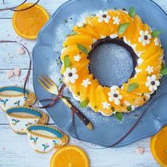 a cake decorated with orange slices and flowers on a blue plate next to some cookies