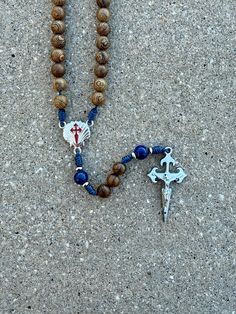 --- 3/4" St. James rosary center --- 1 7/8" St. James crucifix --- 8mm Lapis stone Our Father beads --- stainless steel accent spacers --- 8mm natural roble wood Hail Mary beads --- navy micro cord  --- lightweight and approximately 17 inches long Please let us know, if you have any questions. Follow us on Instagram and Facebook @sistersinchristrosaries to see our latest designs. Please note that colors may differ slightly from how they appear on your screen due to varying monitor settings. Also, due to the nature of natural wood beads and gemstones, variety in wood grain pattern and coloration is to be expected. Adjustable Rosary With Miraculous Medal And Crucifix, Adjustable Rosary With 8mm Beads In Cross Shape, Divine Mercy Chaplet, Wood Grain Pattern, Lapis Stone, Our Father, Hail Mary, Rosary Catholic, St James