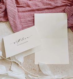 two white envelopes sitting next to each other on top of a pink sheet of paper