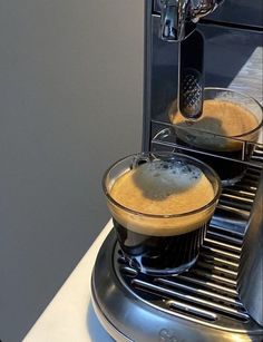 an espresso machine with two cups filled with liquid sitting on top of it