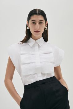 This luxe sleeveless shirt in 100% Cotton boasts a confident silhouette with wide shoulders, and front ruffle detail. The style has a concealed button front opening and is available in Ice Blue or White colour. Colour: White Fit: Loose fit silhouette. Model is wearing a Size AU 8 Fabric & CareMain: CottonGentle machine wash Shipping Information White Shirt Details, White Shirt Designs, Luxury White Top With Contrast Collar, Exaggerated Collar Shirt, Luxury Button-up Tops With Details, Modern White Button-up Top, Shirt Collar Design, Sleeveless Button Up Shirt, Deconstructed White Shirt