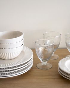 a table topped with white plates and glasses on top of a wooden table next to a wall