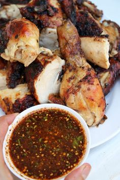 a person holding a white plate with some chicken on it and dipping sauce in the bowl