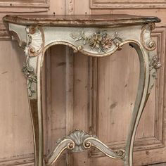 an antique console table with flowers painted on the top and gold trimmings, in front of a wooden paneled wall