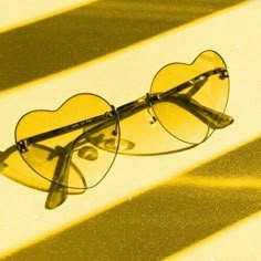 a pair of heart shaped glasses sitting on top of a yellow surface with the sun shining through it