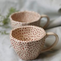 two coffee mugs sitting next to each other on a white cloth covered tablecloth