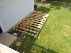 a wooden bed frame sitting on top of a grass covered yard next to a building