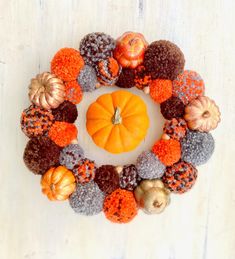 a wreath made out of knitted pumpkins and acorns on a white wooden surface