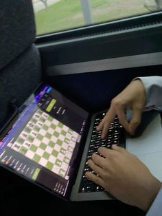 a person using a laptop computer on a seat in a vehicle or bus, with the screen showing chess