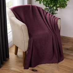 a chair with a blanket on it next to a potted plant in a living room