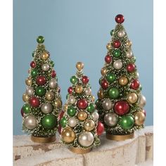 three small christmas trees sitting on top of a stone wall next to each other with ornaments around them