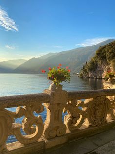 a balcony overlooking the water and mountains with flowers in vases on it's railing