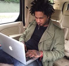 a man with dreadlocks sitting in the back seat of a car using a laptop computer