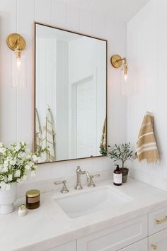 a bathroom sink with a large mirror above it and flowers in the vase on the counter