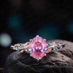 a pink ring sitting on top of a rock with green and blue stones around it