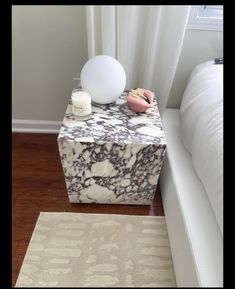 a marbled end table with candles on it next to a bed