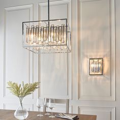 a chandelier hanging over a dining room table with wine glasses and flowers on it