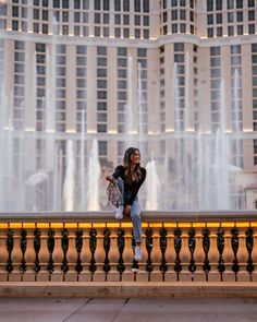 a woman is sitting on a railing with her skateboard in front of a fountain