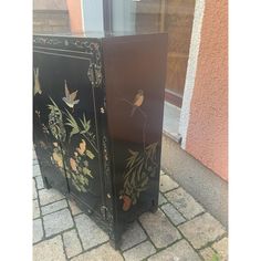 a black cabinet with flowers and birds painted on the doors is sitting in front of a building