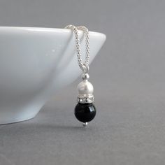 Simple and elegant in design, this black onyx and white pearl necklace would be ideal for bridesmaids in a monochrome themed wedding. A lone, white glass pearl sits in a crystallised band above a jet black onyx bead. This glass pearl and crystal teardrop hangs from a Sterling silver corb chain.  The 18 inch corb chain is a more ornate alternative to the standard snake chain. The way the chain is cut and assembled means it really glimmers in the light. The pearl drop pendant measures 2.3cm high a Black Pearl Drop Necklace For Gift, Elegant Black Pearl Necklace For Weddings, Elegant Black Bridal Necklace For Formal Occasions, Elegant Black Pendant Pearl Necklace, Elegant Black Pearl Necklace For Gift, Elegant Black Pearl Drop Necklace, Elegant Black Drop Necklace Gift, Black Pearl Drop Jewelry For Anniversary, Formal Black Necklace With Pearl Pendant