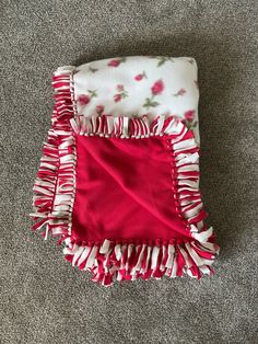 a red and white blanket laying on top of a gray floor next to a pillow