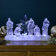 an illuminated nativity scene with figurines and pine cones on a wooden table