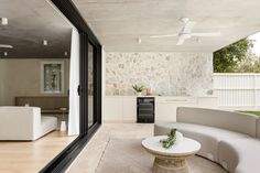 an outdoor living room with white furniture and stone wall behind the couches, as well as a large sliding glass door that leads outside