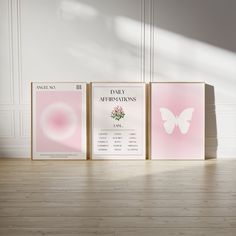 three pink posters are on the floor in front of a white wall and wooden floor