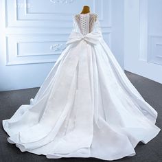 a white wedding dress on display in front of a wall with an open back and large bow