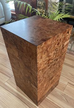 a wooden box sitting on top of a hard wood floor next to a potted plant