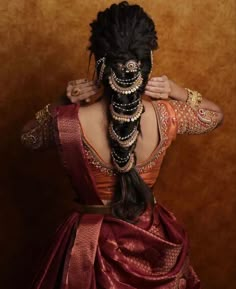 a woman with long hair wearing a red and gold sari, holding her hands behind her head