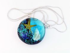 If you love the ocean, you can't help but love this unique pendant of ours, which represents the seabed. Handcrafted from beautiful olive wood and blue clear epoxy resin, this pendant captures the serene beauty of the marine world, with starfish and shells within the resin. It is the perfect accessory for anyone who loves the sea. Whether you're searching for a unique birthday gift or looking to add a touch of the ocean to your outfit, this ocean-inspired pendant is the perfect choice. Its disti Ocean-inspired Blue Pendant Necklace, Ocean-inspired Pendant Necklace, Blue Resin Ocean-inspired Necklaces, Blue Resin Necklaces With Ocean-inspired Style, Ocean-inspired Turquoise Round Pendant Necklace, Blue Resin Ocean-inspired Necklace, Ocean-inspired Blue Resin Jewelry, Blue Ocean-inspired Resin Jewelry, Marine World