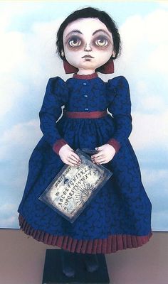 a doll is dressed in blue and holding a silver box with writing on it's face