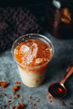 an orange drink in a plastic cup with ice and cinnamon on the table next to it