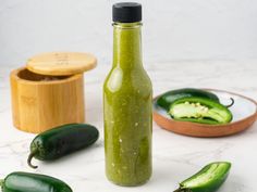 a bottle filled with green liquid sitting next to some sliced jalapeno peppers