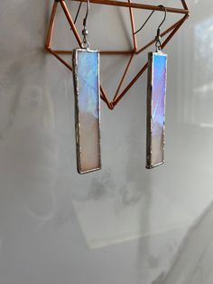 a pair of earrings hanging from a metal bar on a wall next to a mirror