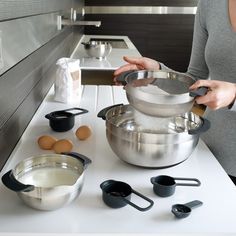 a woman mixing ingredients in a bowl on top of a counter next to pots and pans