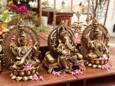 three brass statues sitting on top of a wooden table next to potted plants and flowers