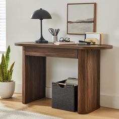 a wooden desk with a lamp and pictures on the wall next to it in a living room