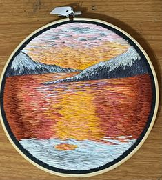 an embroidery project with mountains and water in the background, on a wooden table top