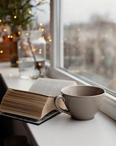 an open book sitting on top of a window sill next to a coffee cup