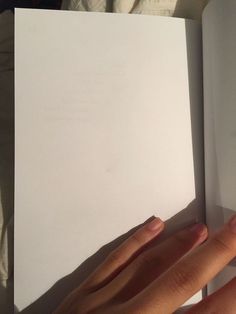 a person's hand holding an open book in their left hand, on top of a white sheet of paper