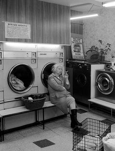 an old woman sitting on a bench in front of a washer and dryer