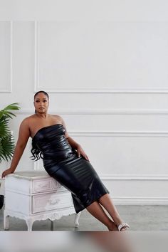 a woman in a black leather dress sitting on a white table