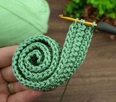 a person holding a green crochet hook with yarn on it and a ball of yarn in the background