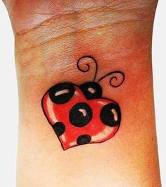 a ladybug tattoo on the wrist that is red with black dots and swirls