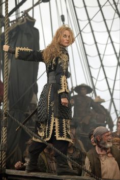 a woman standing on top of a boat in front of other people wearing pirate costumes