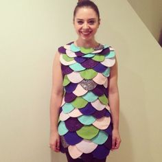 a woman standing in front of a wall wearing a dress made out of paper plates